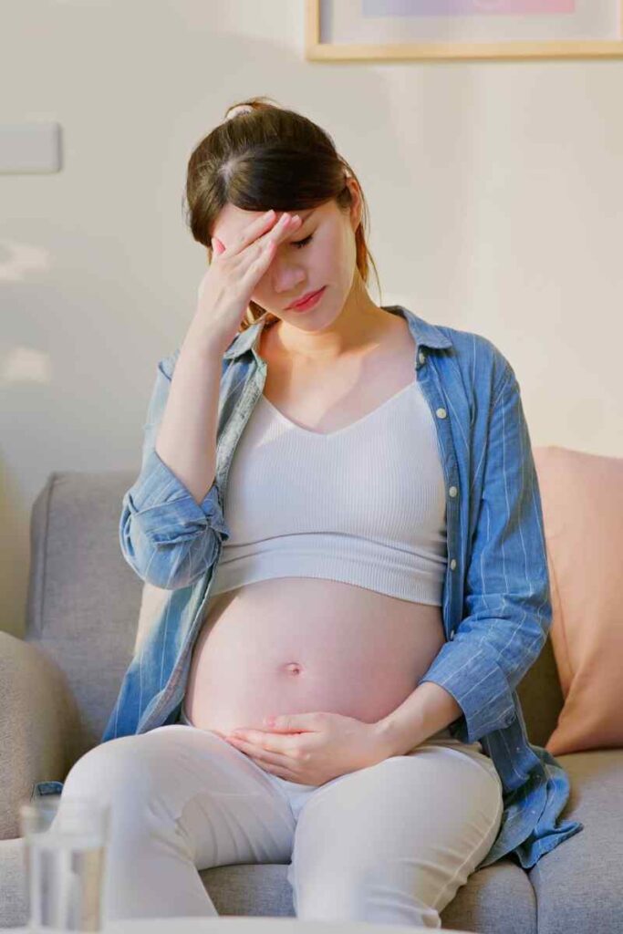 Mulher grávida sentada no sofá com expressão triste, segurando a barriga, representando os sintomas de depressão e ansiedade na gravidez